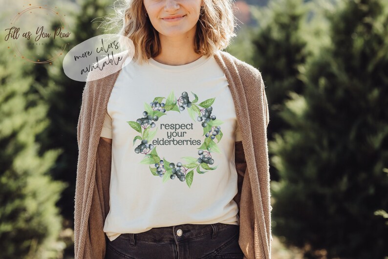 Op de afbeelding: Een wit T-shirt met een aquarelontwerp van vlierbessen en de tekst "respecteer je vlierbessen".