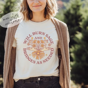 May include: A white t-shirt with a pink and yellow graphic design that says "Will Burn Sage and Bridges as Needed".