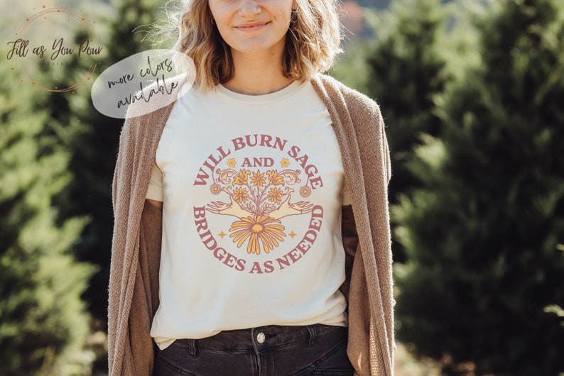 May include: A white t-shirt with a pink and yellow graphic design that says "Will Burn Sage and Bridges as Needed".