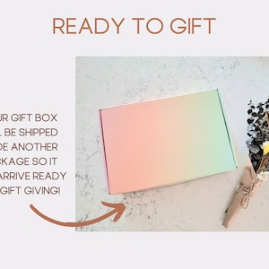 May include: A pastel pink, orange, and green gift box with a bouquet of dried flowers wrapped in brown paper. The text "READY TO GIFT" is above the image. The text "YOUR GIFT BOX WILL BE SHIPPED INSIDE ANOTHER PACKAGE SO IT WILL ARRIVE READY FOR GIFT GIVING!" is to the left of the image. The text "Fill as You Please" is below the image.