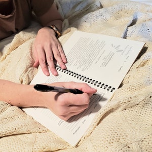 May include: A person writing in a spiral bound journal with a black pen. The journal has the text "day 3" and "birth" on the cover. The journal is open to a page with the text "Describe your labor and delivery".