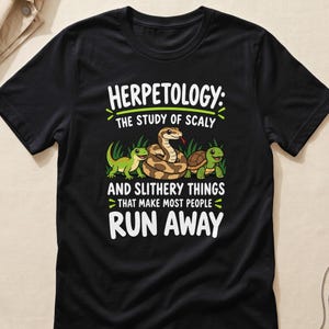 Puede incluir: Una camiseta negra de manga corta con un gráfico de un lagarto verde, una serpiente marrón y una tortuga. El texto dice: HERPETOLOGY: THE STUDY OF SCALY AND SLITHERY THINGS THAT MAKE MOST PEOPLE RUN AWAY, impreso en letras blancas y verdes.