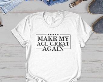 May include: White t-shirt with black text that reads "MAKE MY ACL GREAT AGAIN" in a box with stars above the text.