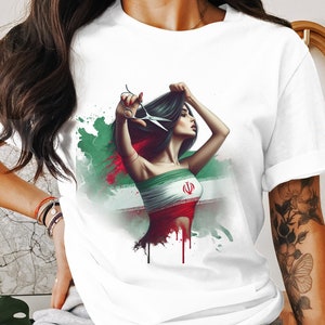 Peut inclure: T-shirt blanc avec un imprimé graphique d'une femme aux longs cheveux noirs tenant des ciseaux devant un drapeau vert, blanc et rouge avec un symbole au centre.