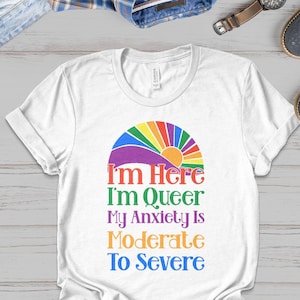 May include: White t-shirt with a rainbow arc and the text "I'm Here I'm Queer My Anxiety Is Moderate To Severe"