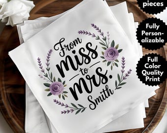 May include: White napkins with the text "From miss to mrs. Smith" in black script, surrounded by a floral wreath with purple roses and green leaves. The napkins are stacked on a wooden tray.