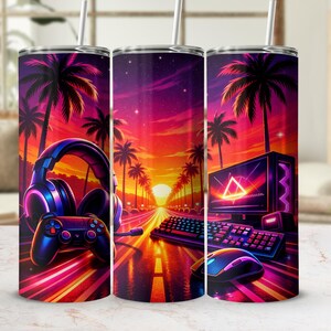 Puede incluir: Un vaso vibrante con un diseño temático de juegos. La obra de arte muestra una escena de atardecer con palmeras, una carretera y accesorios de juego como auriculares, un controlador, un teclado y un ratón. La paleta de colores incluye tonos de morado, naranja y rosa.