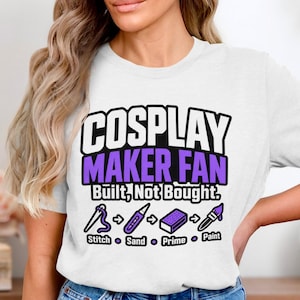 Könnte beinhalten: Ein weißes Kurzarm-T-Shirt mit dem Text "COSPLAY MAKER FAN Built, Not Bought." und einer grafischen Abfolge von Nadel, Schleifgerät, Block und Pinsel mit den Beschriftungen "Stitch", "Sand", "Prime" und "Paint" in Lila und Schwarz.