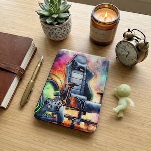 May include: A gaming-themed mousepad featuring a watercolor design of a gaming chair, controller, and headphones. The mousepad has a colorful background with a black and blue chair. A controller is in the foreground.