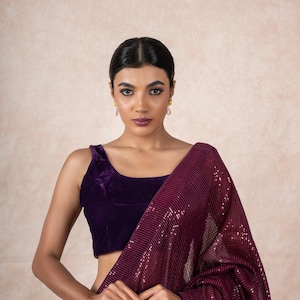 May include: A woman wearing a purple velvet blouse and a maroon sequined saree. The saree is draped over her shoulders and waist.