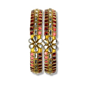 May include: Two gold bangles with red and white square-shaped stones and a flower design.