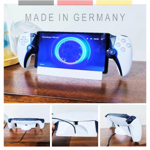 Könnte beinhalten: Ein weiß-schwarzer Gaming-Controller-Ständer mit einem Tablet, das eine blau-weiße Grafik anzeigt. Der Ständer hält das Tablet und zwei Controller. Der Text "MADE IN GERMANY" steht oben.