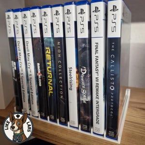 Könnte beinhalten: Ein weißer Kunststoff-Präsentationsständer mit neun PlayStation 5-Videospielhüllen in einer Reihe. Die Buchrücken zeigen Titel wie Gran Turismo 7, Devil May Cry 5 Special Edition, Back 4 Blood, Returnal, Nioh Collection, Steelrising, Demon's Souls, Final Fantasy VII Remake Intergrade und The Callisto Protocol.
