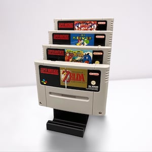 Könnte beinhalten: Ein schwarzer Kunststoff-Präsentationsständer mit vier vertikal gestapelten grauen Super Nintendo-Spielkassetten. Die Etiketten zeigen The Legend of Zelda: A Link to the Past, Yoshi's Island, Super Mario World und Street Fighter II.