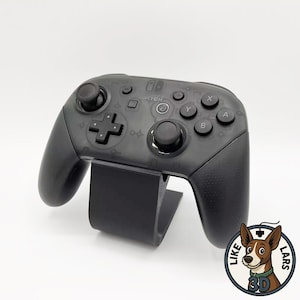 Könnte beinhalten: Ein schwarzer, durchscheinender Nintendo Switch Pro Controller mit Steuerkreuz, zwei Analogsticks und Standard-Aktionstasten, der auf einem schwarzen U-förmigen Ständer ruht. Das Gehäuse zeigt dezente eingravierte Muster und das Switch-Logo.