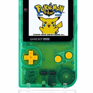 May include: A translucent green handheld game console featuring a screen displaying the Pokémon Yellow Version logo with Pikachu. The device has a yellow directional pad, two yellow action buttons, and the text GAME BOY pocket printed below the screen.