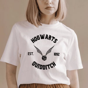 May include: White t-shirt with a black graphic of the Hogwarts Quidditch team logo. The logo features a flying snitch, the words "Hogwarts" and "Quidditch", and the text "Est. 1092".