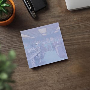 May include: Square sticky note with an illustration of a skeleton sitting at a desk in an office setting. The artwork is in shades of blue and purple. A pen, a small plant, and a laptop are also visible.