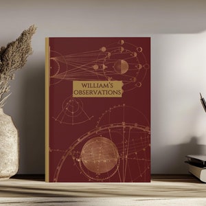 May include: A burgundy hardcover journal with a gold illustration of a celestial map and the text "WILLIAM'S OBSERVATIONS" on the front cover.