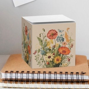 May include: A floral notepad with a bouquet of colorful flowers, including red poppies, yellow daisies, and blue forget-me-nots. The notepad is on a table with two notebooks.