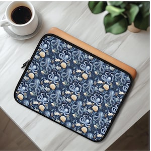 Könnte beinhalten: Eine Laptop-Hülle mit marineblauem Hintergrund und einem sich wiederholenden Muster aus blauen Oktopussen, Muscheln und Wasserpflanzen. Die Hülle hat einen schwarzen Reißverschluss und einen lederfarbenen Rand.