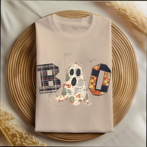 May include: Beige t-shirt with the word "BOO" in patchwork letters. The "B" is plaid, the ghost is floral, and the "O" is geometric. The design is stitched onto the shirt, creating a unique, handmade look. Perfect for Halloween.
