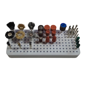 Puede incluir: Una colección de brocas y accesorios para herramientas rotativas, que incluye varios cabezales de cepillo, piedras de amolar y brocas, dispuestos en una bandeja de almacenamiento blanca. Las brocas presentan elementos negros, dorados, plateados, rojos y verdes.