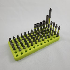 May include: A collection of screwdriver bits and sockets displayed in a bright green holder. The bits are silver and grey, with yellow detailing. The holder is rectangular with numerous holes to accommodate the bits.