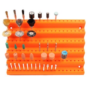 May include: An orange tiered organizer filled with various rotary tool bits. The bits include grinding stones, drill bits, and wire brushes. The organizer has multiple holes for holding the bits.
