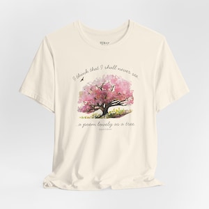 May include: Cream-colored t-shirt featuring a watercolor illustration of a tree with pink blossoms. The text "I think that I shall never see... a poem lovely as a tree" is printed above and below the tree. The brand name "Iliker" is printed at the top.