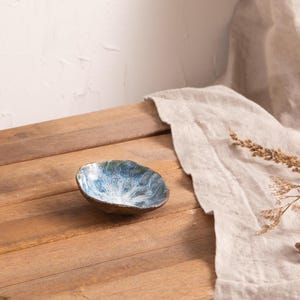 Könnte beinhalten: Eine kleine, blaue und weiße Keramikschale mit einem welligen, abstrakten Design. Die Schale steht auf einer Holzoberfläche.