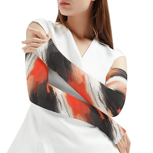 Puede incluir: Mangas de brazo con un diseño abstracto en negro, blanco y naranja. Las mangas presentan audaces pinceladas. Se usan sobre una prenda blanca, creando un contraste llamativo. Diseñadas para cubrir los brazos.