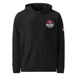 Peut inclure: Sweat-shirt à capuche noir avec un logo circulaire blanc qui dit "Vintage Detroit Techno" en lettres rouges, blanches et bleues.