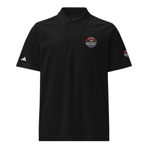 Peut inclure: Polo noir avec un logo Adidas blanc sur la manche gauche. Le polo a un logo circulaire sur la poitrine droite avec le texte "Vintage Detroit Techno" en blanc.