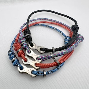 May include: Three braided rope bracelets with metal chain links and black metal beads. The bracelets are in blue, red, and black.