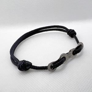 May include: A black braided cord bracelet with a silver bike chain link accent.