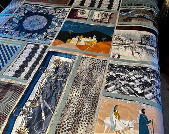 May include: A patchwork quilt made from various fabrics, including a blue and white paisley print, a black and white geometric print, and a beige and brown animal print. The quilt is laid out on a bed with a wooden headboard.
