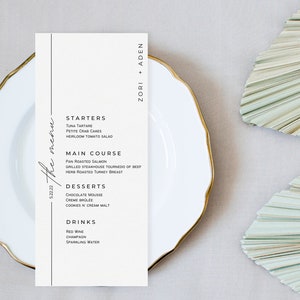 May include: A white menu card with a black vertical line on the left side. The menu card lists starters, main course, desserts, and drinks. The text at the top of the card reads "Zori + Aden" and the text at the bottom reads "5.22.22 the menu".