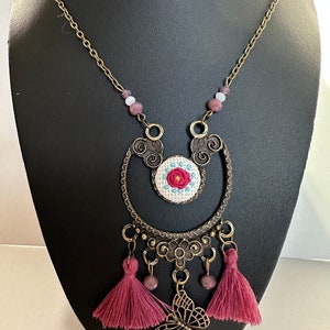 May include: A gold chain necklace with a pink and white embroidered flower charm, a butterfly pendant, and pink tassels.