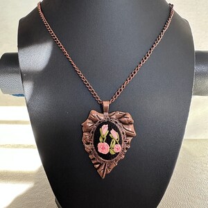 May include: A copper chain necklace with a pendant featuring a black velvet heart-shaped frame with a pink rose embroidery design.