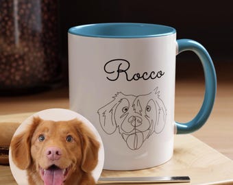 May include: White ceramic mug with a blue rim and handle. The mug has a black line drawing of a dog's face and the name "Rocco" written in cursive. A photo of a brown dog is in the foreground.