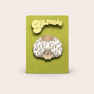 May include: A whimsical pin featuring a cartoon character with a fluffy, white and brown afro and sunglasses. The pin is set against a green background with the word "SHRIMERS" in a yellow, stylized font.