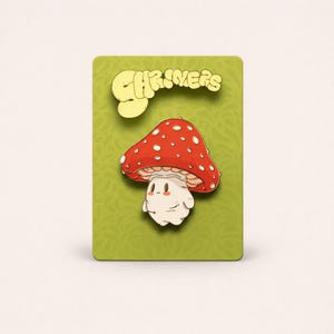 May include: A whimsical mushroom enamel pin with a red cap dotted with white spots. The mushroom has a cute, smiling face and is set against a green background. The word "CHRIVERS" is displayed in yellow above the mushroom.