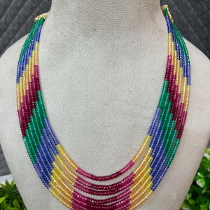 Puede incluir: Un collar de múltiples hilos con pequeñas cuentas redondas facetadas en un patrón de colores repetitivo de azul, amarillo, magenta y verde. Los hilos están dispuestos en un diseño en cascada, creando una apariencia vibrante y texturizada.