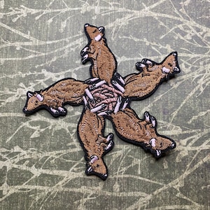 May include: A brown embroidered patch of five mice in a circle, with their tails pointing outwards. The mice are brown with pink noses and ears.