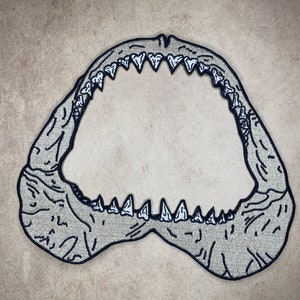 May include: A black and white embroidered patch of a shark's open mouth with rows of sharp teeth.
