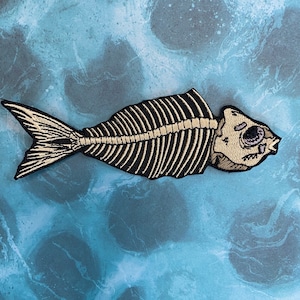 May include: A black and gold embroidered patch of a fish skeleton on a blue background.