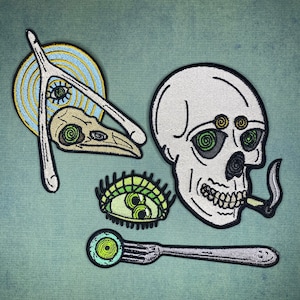 May include: Five embroidered iron-on patches featuring a skull with a cigarette, a bird skull with an eye, a spiral eye, a single eye with eyelashes, and a fork with a spiral eye.