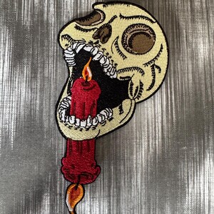 May include: A white skull with an open mouth and a red candle inside. The candle has a yellow flame.