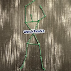 May include: Green embroidered patch with a constellation design and the text "Anomaly Detected" on a white banner.